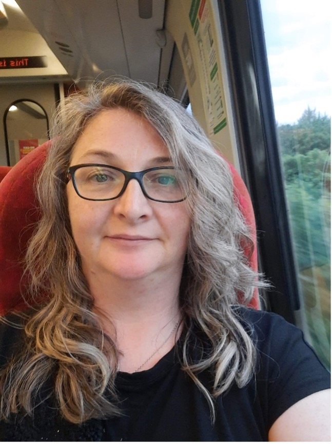 A woman with glasses and long hair sat on a train.