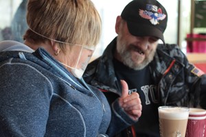 A man and a woman sat in a cafe. The woman is giving a thumbs up. 