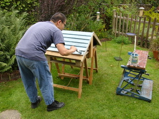 Chif working on building a bug hotel. He's painting the roof in the garden.