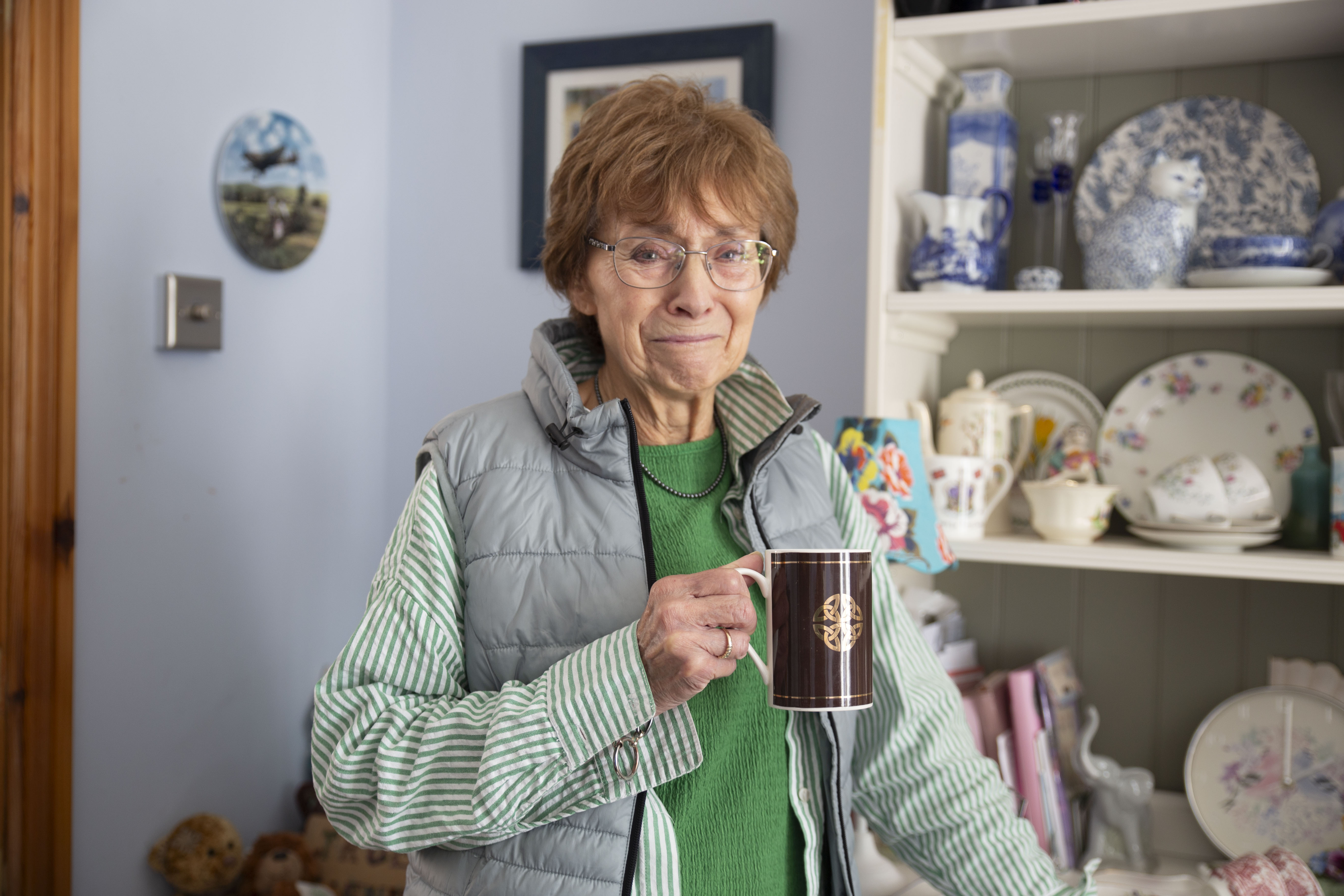 An older woman at home smiling with a cup of tea
