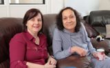 Shirley and her support worker smiling at the camera sat on arm chairs. 
