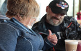 A man and a woman sat in a cafe. The woman is giving a thumbs up. 