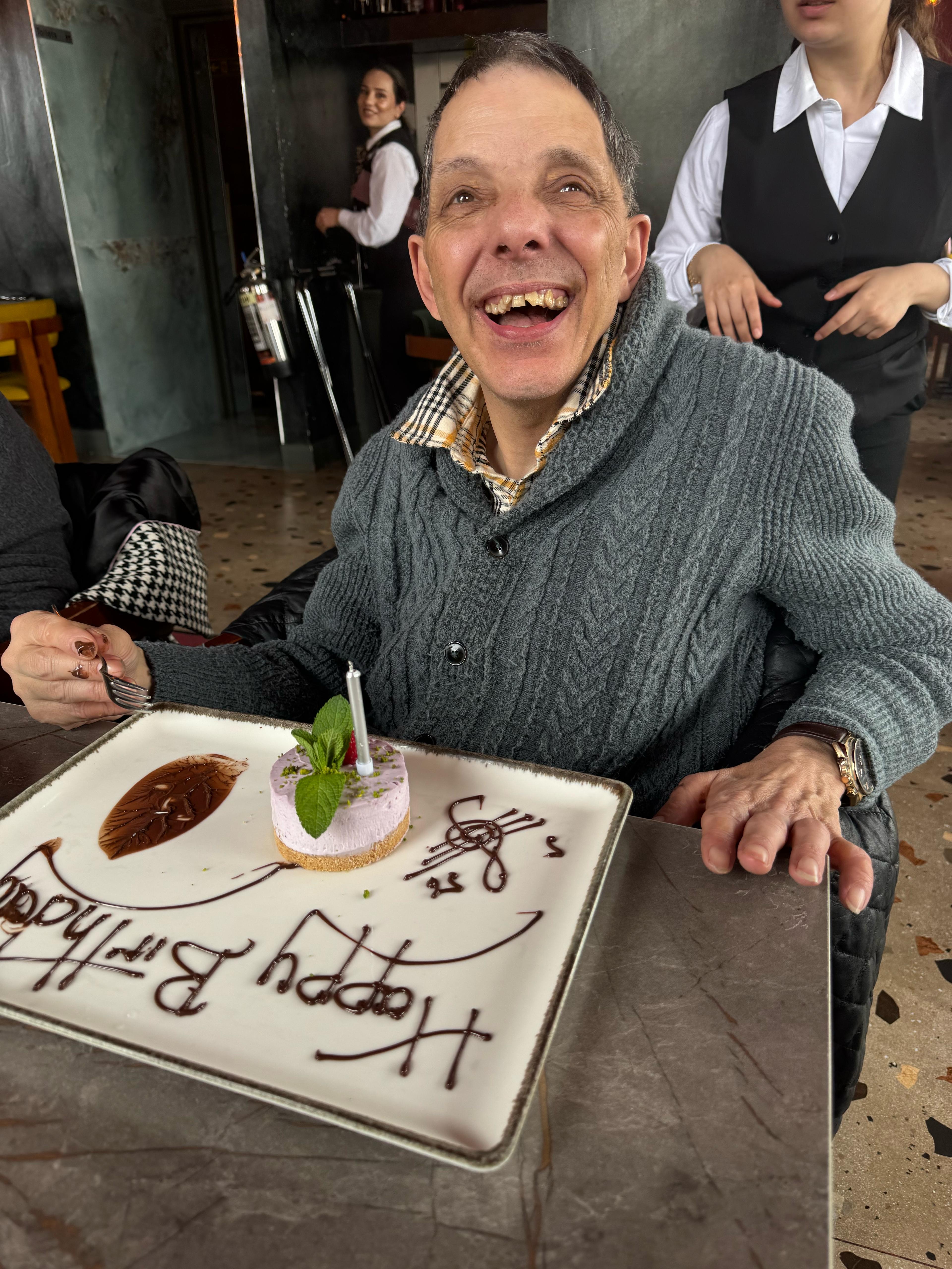 A man smiling at the camera with a birthday cake in front of him