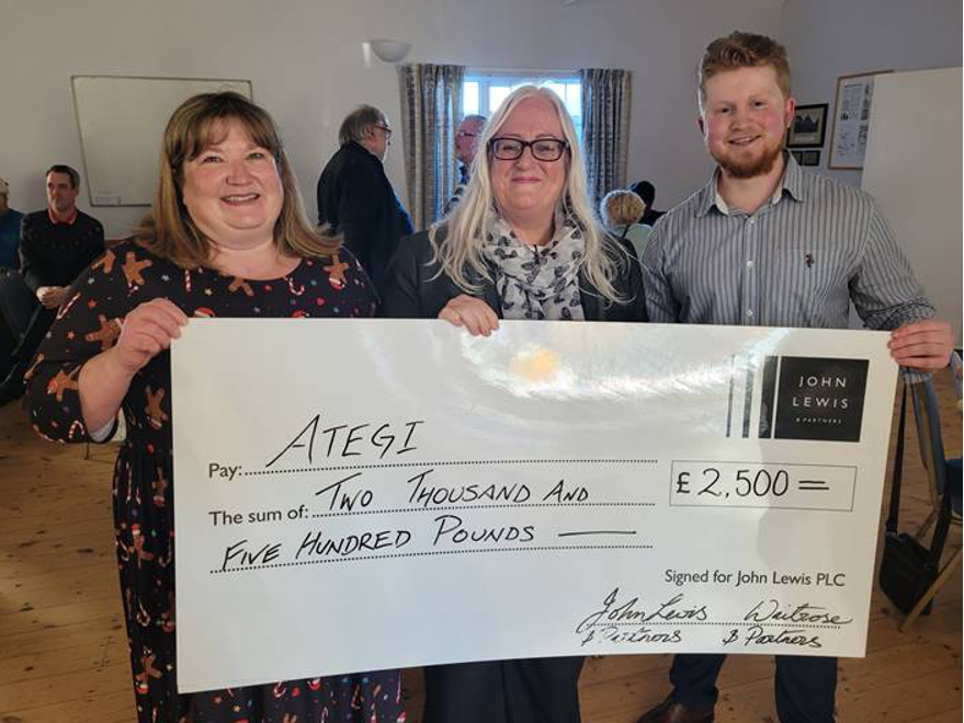 three people holding a giant cheque fro £2,500. Presented to Ategi by John Lewis & Waitrose