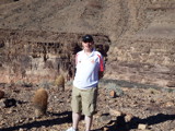 A man wearing a football shirt stood a barren rocky landscape. 