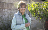 An older lady stood in a sunny garden smiling. 