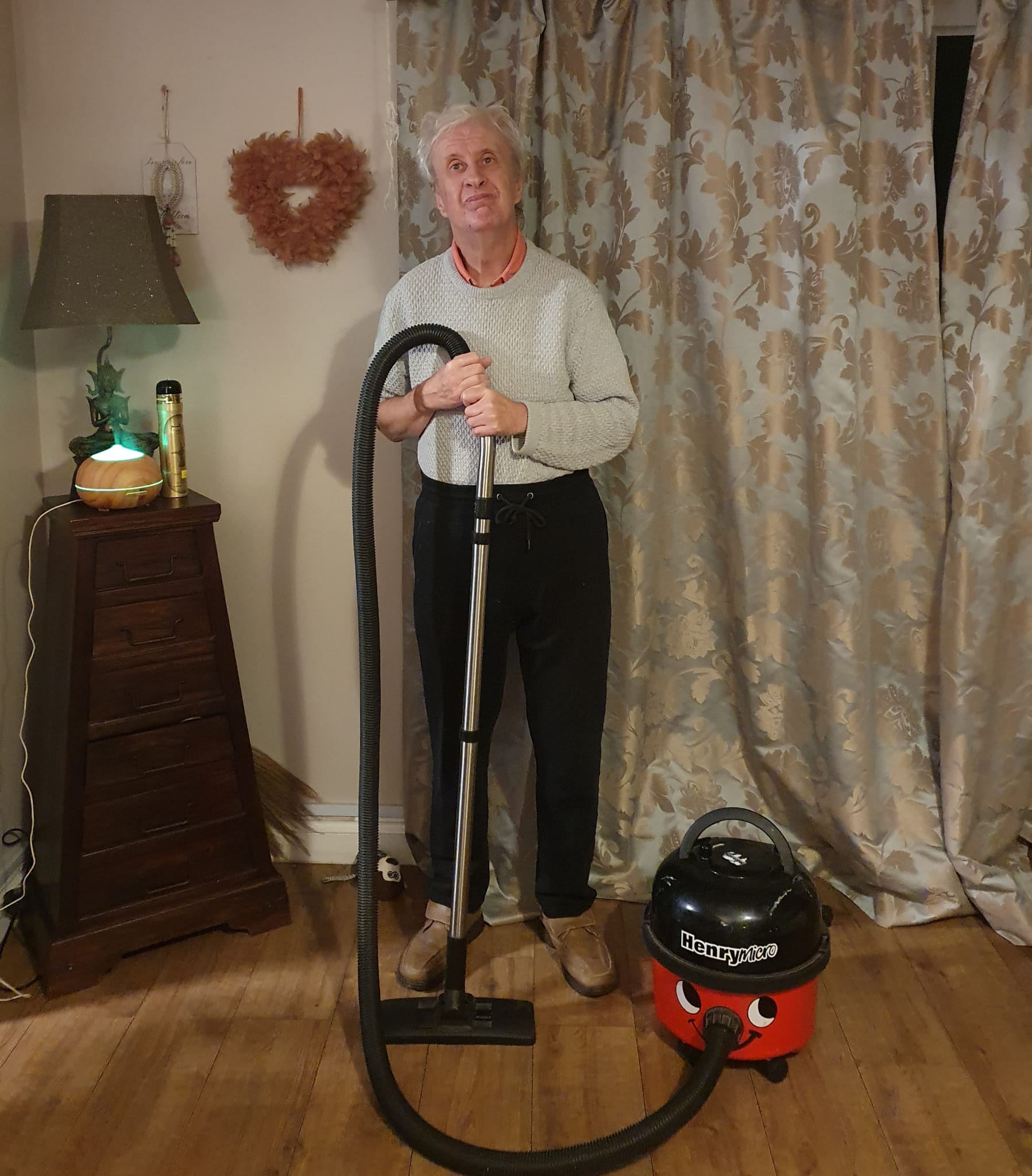 A man stood in a living room proudly holding a Henry Hoover