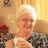 Grazelda, Shared Lives carer, drinking a cup of tea and smiling. 