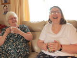 An older woman and younger woman sat together at home laughing