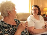 Wendy having a cup of tea with her Shared Lives carer, Grazelda. Both women are smiling. 
