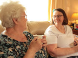 Wendy having a cup of tea with her Shared Lives carer, Grazelda. Both women are smiling. 